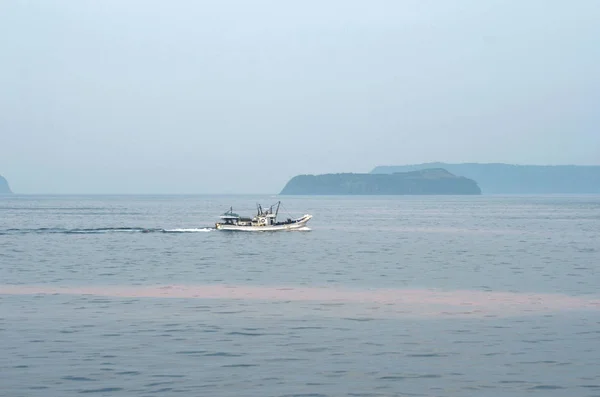 Un barco pesquero pasando por algunas islas, con el agua rosada de una floración de algas . — Foto de Stock