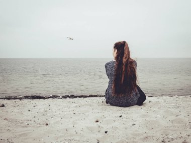 Sevimli genç kadın kum plaj üzerinde oturur ve mesafe içine bakıyor
