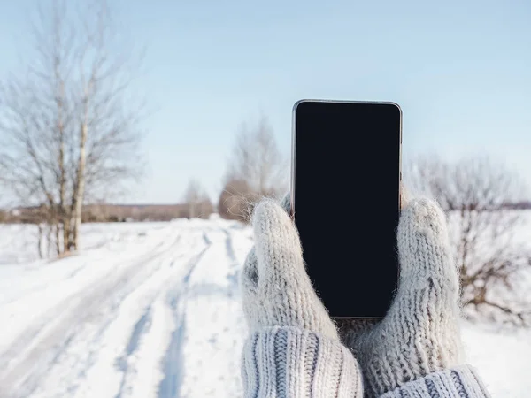 Woman holding a mobile phone in woolen mittens