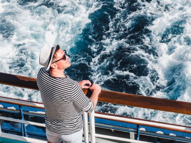 Deniz dalgalarının arka planında bir yolcu gemisinin boş güvertesinde gülümseyen adam. Üst teregörüş, yakın çekim. Eğlence ve seyahat kavramı