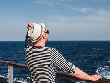 Deniz dalgalarının arka planında bir yolcu gemisinin boş güvertesinde gülümseyen adam. Üst teregörüş, yakın çekim. Eğlence ve seyahat kavramı