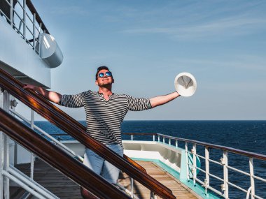 Deniz dalgalarının arka planında bir yolcu gemisinin boş güvertesinde gülümseyen adam. Üst teregörüş, yakın çekim. Eğlence ve seyahat kavramı