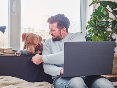 Yakışıklı bir adam ve sevimli bir köpek yavrusu. Evden çalışmak. Yakın plan, kapalı mekan. Stüdyo fotoğrafı, beyaz renk. Bakım, eğitim, itaat eğitimi ve evcil hayvan yetiştirme kavramı