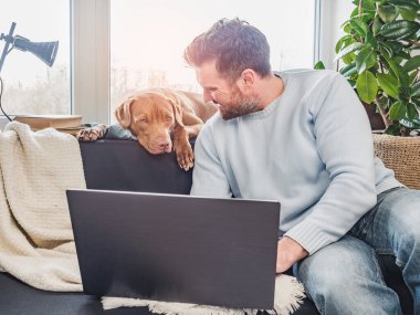 Yakışıklı bir adam ve sevimli bir köpek yavrusu. Evden çalışmak. Yakın plan, kapalı mekan. Stüdyo fotoğrafı, beyaz renk. Bakım, eğitim, itaat eğitimi ve evcil hayvan yetiştirme kavramı