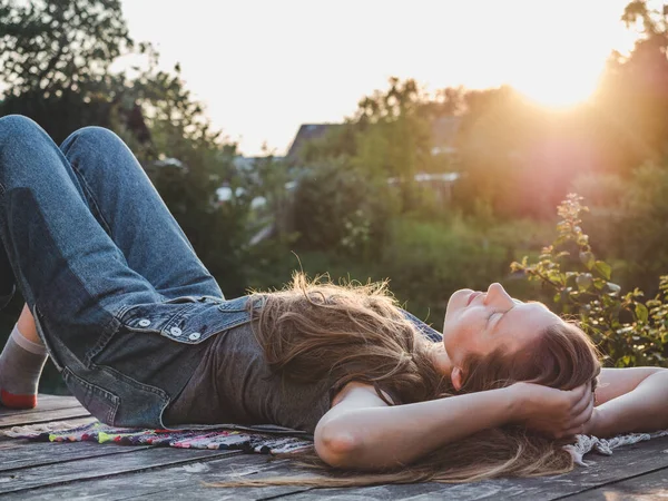 Pretty woman lying on a wooden terrace at sunset background. Closeup, side view, outdoor. Concept of rest and relaxation