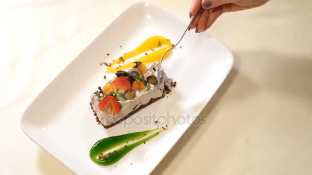 Interior del restaurante. San Valentín. Vista superior del plato con pastel de crema con fresa y otras bayas. La mano femenina con un tenedor rompe un trozo. Disparo en 4k — Vídeos de Stock