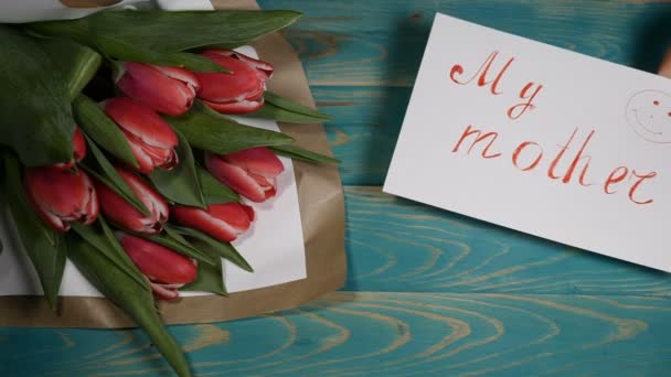 Vista superior de uma nota de mensagem Minha Mãe e buquê de flores de tulipas em uma mesa de madeira. Conceito de relacionamento amoroso. Dia da mãe. Tiros em 4K — Vídeo de Stock