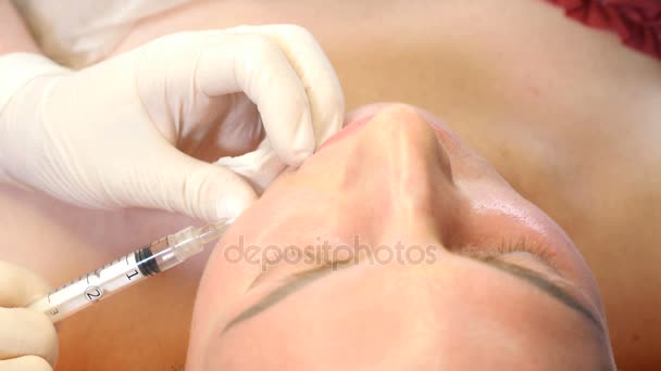 Conceito de clínica de beleza. Close-up de mãos esteticistas fazendo injeção de botox nos lábios femininos. Uma jovem recebe um procedimento de injecção facial, um rejuvenescimento facial. 4k — Vídeo de Stock