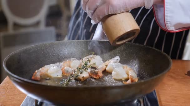 Primer plano de un chef que prepara un plato estilo Flambe en una sartén. En cámara lenta. El aceite y el alcohol se encienden con llamas abiertas. Cocinar y añadir pimienta a los camarones tigre. Disparo en 4k — Vídeo de stock