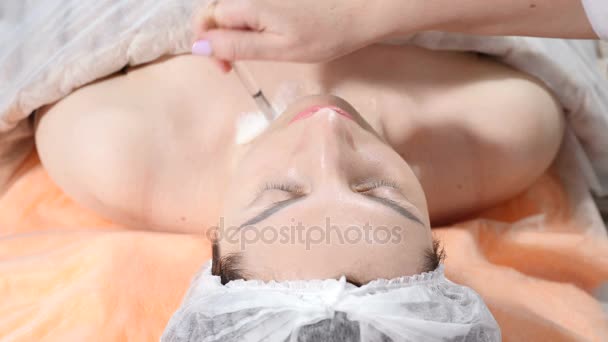 Beauty kliniken koncept. Närbild av kosmetolog händer sprider rengöring mask med en borste till kvinnliga ansikte före injektion. Ung kvinna blir facial förfarande. Facial föryngring. Sköt i 4k — Stockvideo