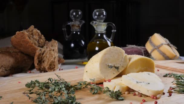 Koncept restaurace. Prostřený stůl. Krájené tvrdé sýry na dřevěné pozadí s domácí pečivo, ořechy a olivových láhve. Zpomalený pohyb — Stock video