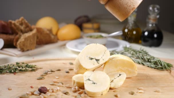 Conceito de restaurante. Configuração da mesa. Queijo duro fatiado colocar em fundo de madeira com pão caseiro, nozes e garrafas de azeitona. Acrescente pimentão. Movimento lento — Vídeo de Stock