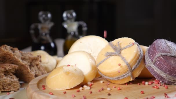 Conceito de restaurante. Configuração da mesa. Queijo duro fatiado colocar em fundo de madeira com pão caseiro, nozes e garrafas de azeitona. As nozes caem. Movimento lento — Vídeo de Stock