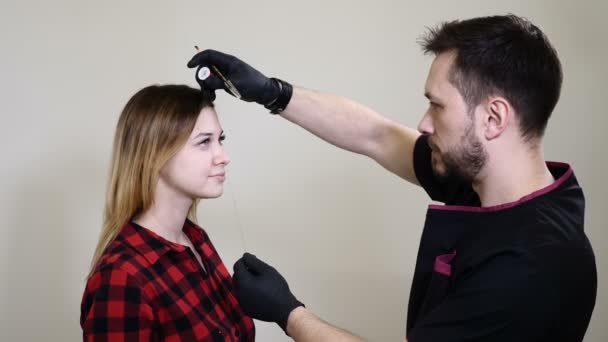 Salone di bellezza. Estetista maschile in guanti neri che applica eyeliner sopracciglio prima della procedura permanente di trucco. Giovane donna ottiene la procedura di bellezza del viso. Ringiovanimento facciale — Video Stock