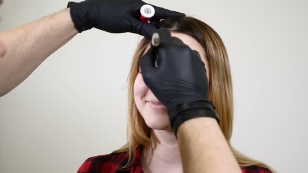 Esthéticienne masculine en gants noirs faisant une procédure de maquillage permanente sur les sourcils féminins. Cosmétologue esthéticienne dans le cabinet de la clinique. ratio d'or en cosmétologie — Video