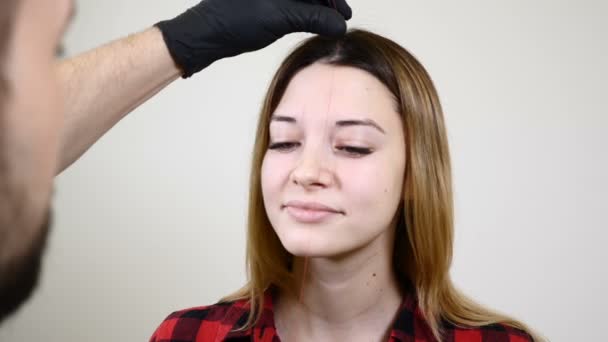 Мужчина косметолог в черных перчатках делает постоянную процедуру макияжа на женских бровях. Косметолог-косметолог в кабинете медицинской клиники. золотое сечение в косметологии — стоковое видео