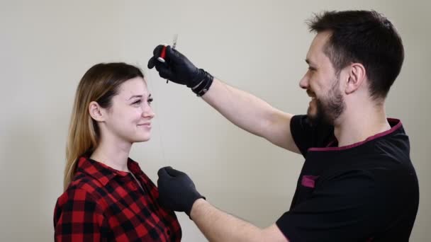 Retrato de cliente mujer feliz y esteticista masculina en el gabinete de la clínica de salud del salón de belleza. Cosmetólogo masculino en guantes negros haciendo procedimiento de maquillaje permanente en las cejas femeninas. Arriba los tambores — Vídeos de Stock