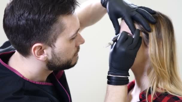 Estética masculina en guantes negros que hace el procedimiento permanente del maquillaje en las cejas femeninas. Cosmetólogo esteticista en el gabinete de la clínica de salud del salón de belleza. usando la regla de la proporción dorada en cosmetología — Vídeos de Stock