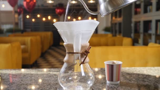 Modern and alternative ways of coffee making.Barista brews coffee using Coffee maker Chemex. Close up of hands pouring hot water out of pot into paper filter with Coffee. Slow motion — Stock Video