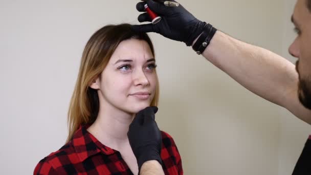 Skönhetsklinik. Manliga kosmetolog i svarta handskar tillämpa ögonbryn eyeliner innan förfarandet för permanent make-up. Ung kvinna blir ansikts skönhet förfarande. Facial föryngring — Stockvideo