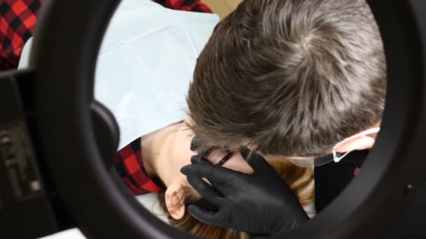Beauty salon. Close up of Male beautician in black gloves making permanent makeup procedure on female eyebrows. Young woman gets facial beauty procedure. Facial rejuvenation. Using tattoo machine — Stock Video