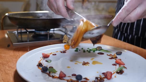 Koken restaurantconcept. De instelling van de tabel. Chef-kok in handschoenen zet flamberen pannenkoeken met karamel op bord versierd met bessen. Slow motion. — Stockvideo