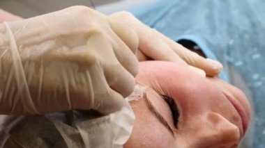 Güzellik Kliniği. Genç kadın istemci iş parçacığı yüz germe alır. Eldiven surat bir kadın yüzü anti-aging güzellik uzmanı