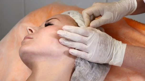 Clínica de salud. Joven cliente femenino obtiene hilo procedimiento de elevación de la cara. esteticista en guantes haciendo cara antienvejecimiento a una cara femenina — Vídeo de stock