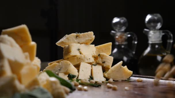 Kunst restaurantconcept. Verschillende soorten kaas plaatsen in hoopjes op houten achtergrond Handvol pijnboompitten in slow motion — Stockvideo