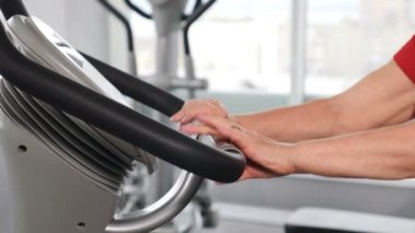 Spor salonunda aktif son sınıf öğrencisi. Kapatın. Fitness stüdyosunda bisiklet kulpunda kadın eller. Bisiklet sınıfında bisiklet süren yaşlı bir kadın. Spor kulübünde statik bisikletle spor yapan yaşlı kadın antrenmanı. 4k
