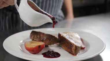 Yemek videosu. Şef pişmiş ördek etinin üzerine koyu sos döküyor. Beyaz tabakta kırmızı armut tatlısıyla servis ediliyor. Düşük hareket. Kapatın. Yüksek çözünürlüklü çekim