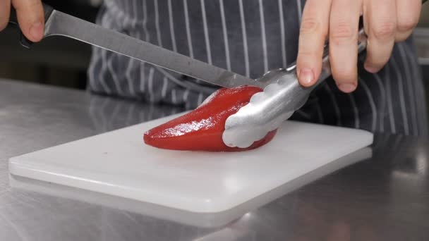 Koki memotong pir yang dimasak dengan anggur merah kering. Makanan penutup pir lezat di dapur restoran. Gerakan lambat. Tutup. Pemotongan pir papan putih disiapkan dalam anggur. hd — Stok Video