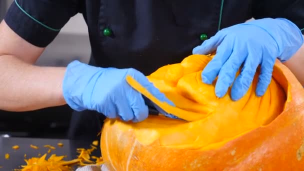 Halloween day preparation. making jack-o-lantern. Hand carves eyes, nose and smile with knife on orange pumpkin. Close up shooting. 4K. — ストック動画