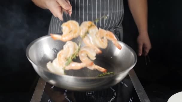 Conceito de cozinha restaurante. Chef joga camarões fritos na frigideira no fundo preto. Chef arremessos, mistura e jogando em camarões pan, close-up câmera lenta. hd — Vídeo de Stock