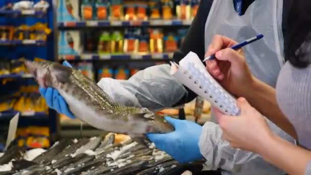 Food supply quality control. Close up. Female hands making notes in shopping list at supermarket while salesman hands showing sevruga starry sturgeon. Choosing food for restaurant. Concept daily — Stock Video