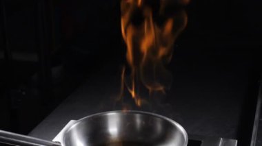 Karanlık arka planda paslanmaz tavadan ateş yükseliyor. Alevli yemek pişirmek. Şef Flambe Stili Tabağı Hazırlama 'nın yakın çekimi. Açık Alevli Yağ ve Alkol Yangını. Ağır çekim. hd