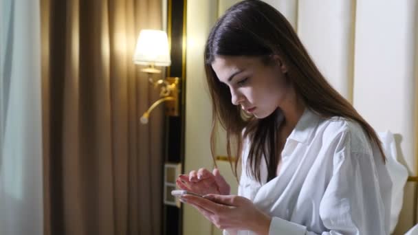 Young attractive woman using cellphone browsing online website shopping before sleep sitting on bed. young girl with mobile phone. technology addicted. texting chatting. 4k — Stock Video