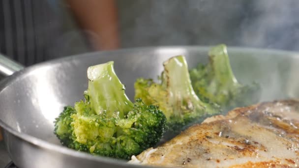 Le feu, la flamme et l'huile éclaboussent au ralenti pendant la cuisson du filet de poisson avec des légumes sur la poêle. Préparation des plats du restaurant. Brûleur à gaz est utilisé pour la cuisson du brocoli et du poisson. Tourné en HD — Video