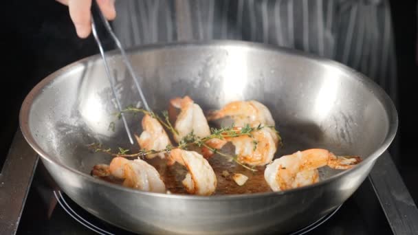 Chutné smažené krevety s kleštěmi na rozpálené pánvi. Kuchař používá kleště k tahání vařené. Nerozpoznatelný kuchař házející pánev a převracející se krevety smažící se v oleji. Zpomal. Hd — Stock video