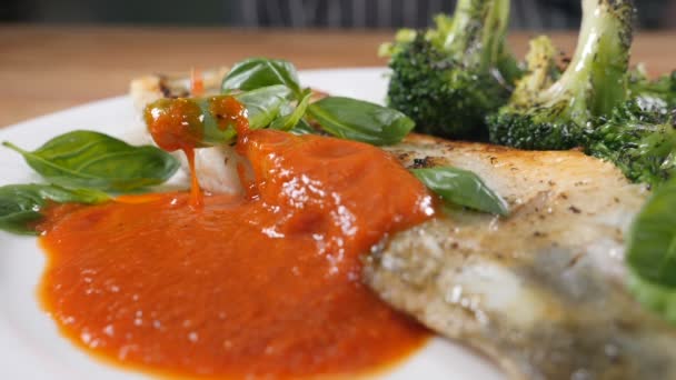Kızarmış balıkla brokoli ile servis edilen beyaz tabakta lezzetli bir sos. Güzel mutfak. Michelin yıldızlı restoranda ağız sulandırıcı yemek. Ağır çekim. Yüksek çözünürlüklü çekim — Stok video