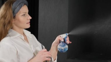 Genç bir kadın suluboya ve ağır çekimde boyaya su püskürterek akvaryum boyasını nemlendiriyor. Resim stüdyosundaki tuvale resim yapan beyaz tişörtlü kadın sanatçı. Kapatın. Hd