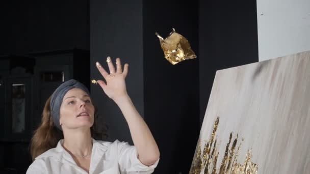 Foglia d'oro che cade al rallentatore. Giovane artista femminile creativa decorare opere d'arte con oro artificiale gettando foglia e soffiando su di esso. Hd — Video Stock