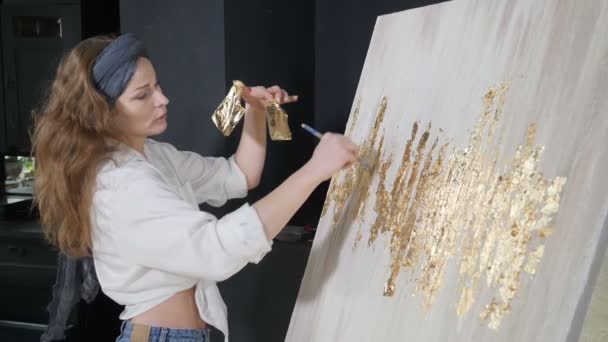 Jeune artiste féminine appliquant la feuille d'or à son œuvre d'art. Artiste décore l'image avec une petite feuille d'or. école d'art, créativité et concept de personnes. Au ralenti. Tourné en HD — Video