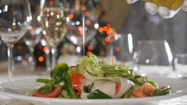 Imagens de vídeo de comida em câmara lenta. Alimentação saudável e conceito vegetariano. close-up tiro de derramamento de azeite sobre salada em restaurante de luxo com luzes de Natal borradas, guirlanda piscando no fundo — Vídeo de Stock