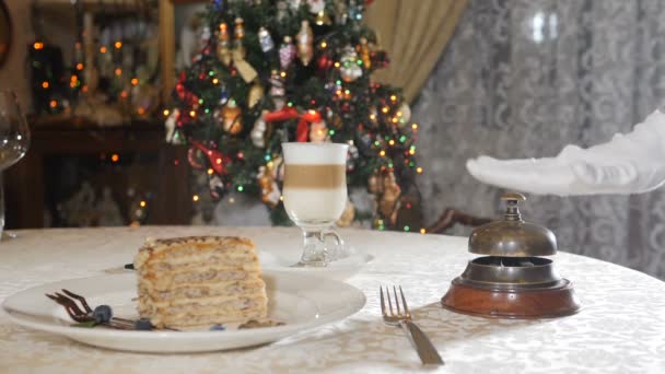 Nowy Rok i świąteczne dekoracje w luksusowej restauracji. nakrycie stołu. Pyszny deser i kawa latte na białym stole. Ręka w białej rękawicy naciskając zabytkowy dzwonek restauracji. Zwolnij trochę. Tłumaczenie: — Wideo stockowe