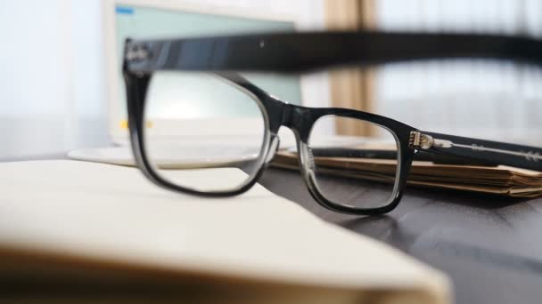 Concept d'entreprise et de bureau. Images filmées à travers une jante noire de lunettes sur un bloc-notes vide. Main masculine emportant tasse de café en arrière-plan. Repose-toi en travaillant dur. Tourné en 4k — Video