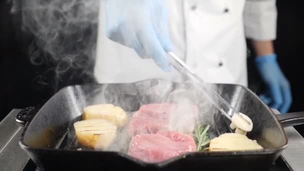 Chef cuisinier de pommes de terre avec de la viande sur le gril à l'aide de pinces pour tourner les pommes de terre sur la plaque chauffante. Fumez au ralenti. hd — Video