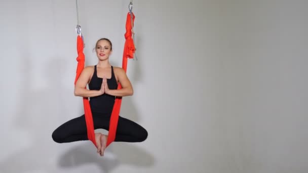 Portrait of young girl at Aero yoga classes sitting on hammock in the air. Shot on white background. In solitude young lady rests and concentrates with eyes closed and palms clasped in a namaste — 비디오