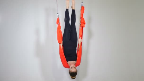 Sporty woman hanging upside down in hammock studio. Atraktivní dívka cvičení antigravitační jóga v bílém pozadí. Krásná fena v černém oblečení intenzivně cvičí v robustním zařízení. Video 4k — Stock video
