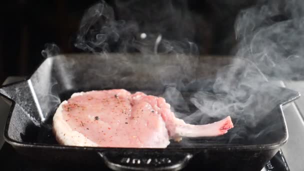 Szef kuchni gotowanie smażone mięso stek na patelni na czarnym tle, para rośnie z naczynia w zwolnionym tempie, jedzenie master klasy, Materiał żywnościowy do reklamy. Zbliżenie — Wideo stockowe